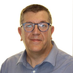 Head-and-shoulders portrait of a middle-aged man with short hair, blue-rimmed glasses, and a light blue shirt, giving a neutral smile.