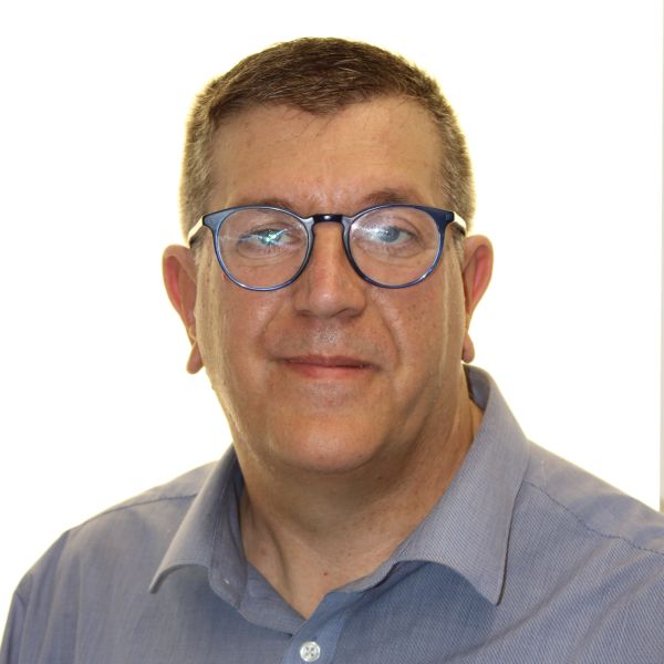 Head-and-shoulders portrait of a middle-aged man with short hair, blue-rimmed glasses, and a light blue shirt, giving a neutral smile.