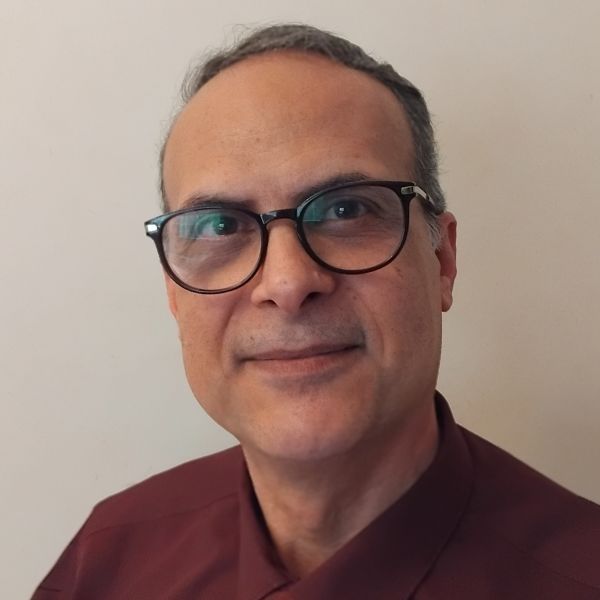 A middle-aged man with dark glasses and short gray hair, wearing a maroon shirt, looking at the camera against a light backdrop.